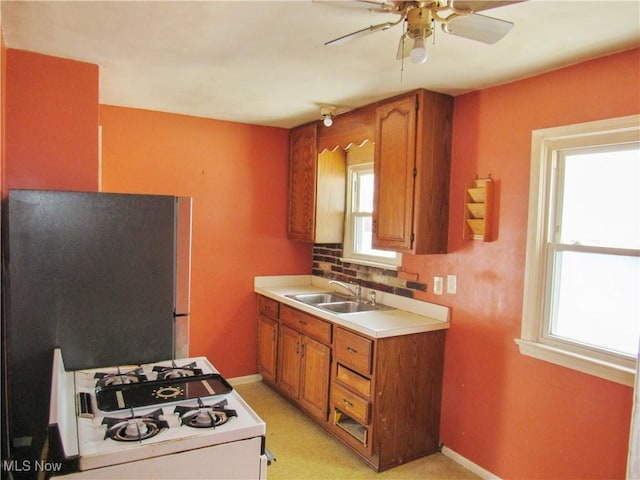 kitchen with sink, decorative backsplash, white range with gas stovetop, light colored carpet, and ceiling fan