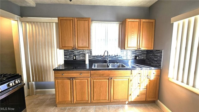 kitchen with sink, gas range, a textured ceiling, light tile patterned floors, and decorative backsplash