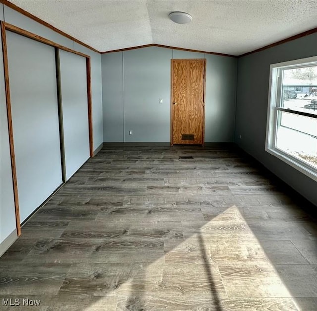 unfurnished bedroom with crown molding, lofted ceiling, a textured ceiling, and light wood-type flooring