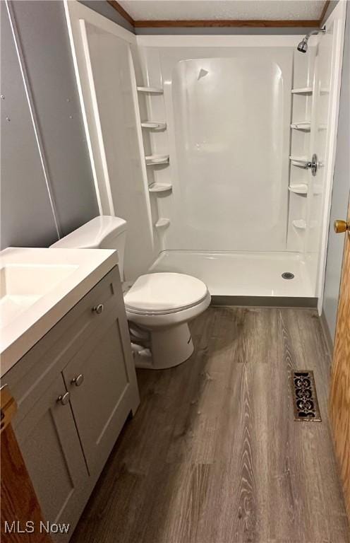 bathroom with crown molding, vanity, wood-type flooring, a shower, and toilet