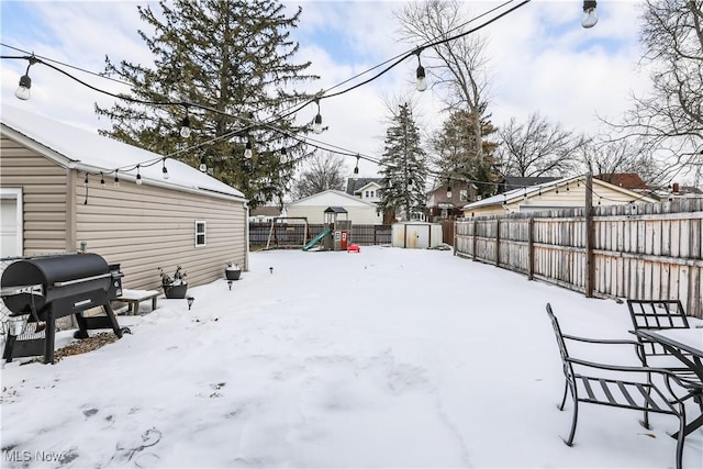 snowy yard with a playground and a storage shed