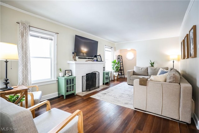 living room with dark wood-type flooring, crown molding, and a brick fireplace