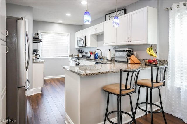 kitchen featuring white cabinetry, hanging light fixtures, dark stone countertops, appliances with stainless steel finishes, and kitchen peninsula