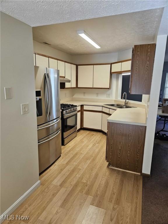 kitchen with appliances with stainless steel finishes, sink, light wood-type flooring, kitchen peninsula, and a textured ceiling