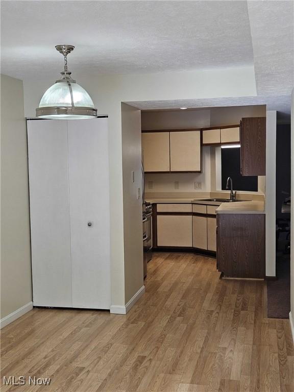 kitchen featuring sink, light hardwood / wood-style flooring, hanging light fixtures, and a textured ceiling