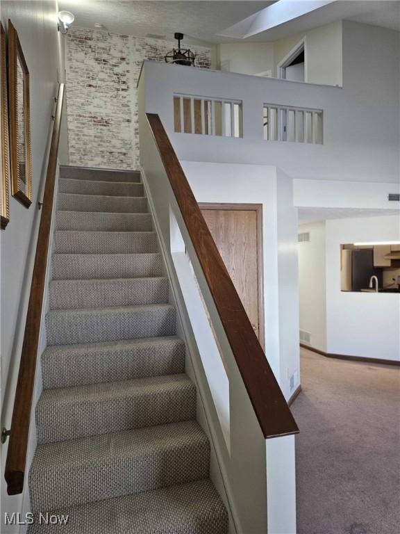 staircase with a high ceiling, carpet flooring, and sink