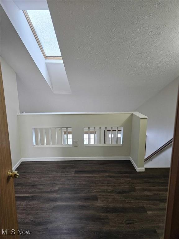 additional living space with dark wood-type flooring, vaulted ceiling with skylight, and a textured ceiling