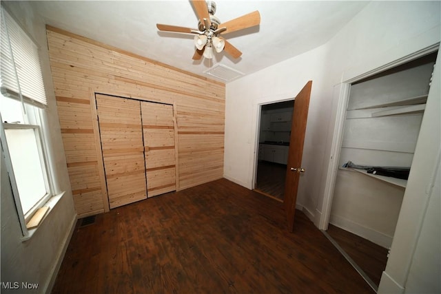 unfurnished bedroom with a closet, dark hardwood / wood-style floors, ceiling fan, and wood walls