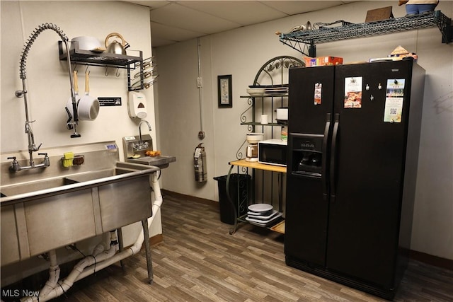 kitchen with a paneled ceiling, black fridge with ice dispenser, and hardwood / wood-style floors