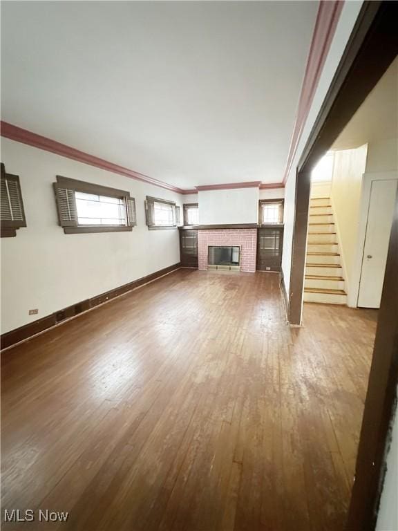 unfurnished living room with a tiled fireplace, ornamental molding, and hardwood / wood-style floors