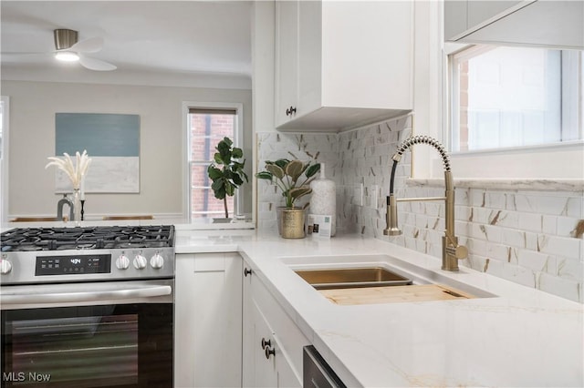 kitchen with white cabinetry, sink, decorative backsplash, light stone counters, and stainless steel gas range oven