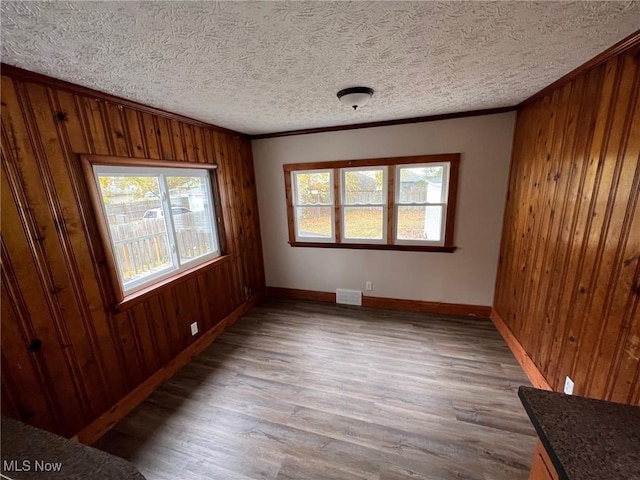 unfurnished room featuring hardwood / wood-style floors, ornamental molding, a textured ceiling, and wood walls