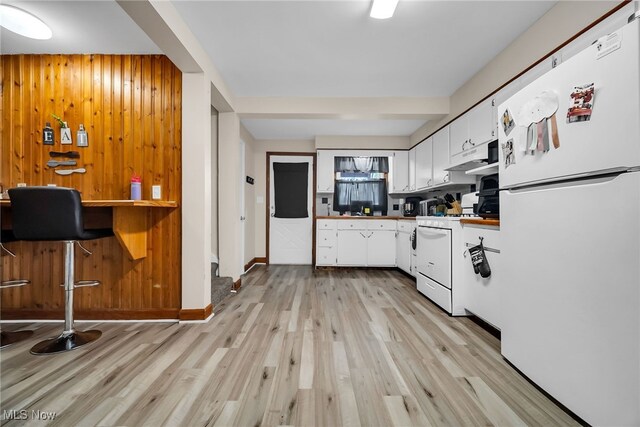 kitchen featuring under cabinet range hood, light wood-type flooring, wooden walls, white cabinetry, and white appliances