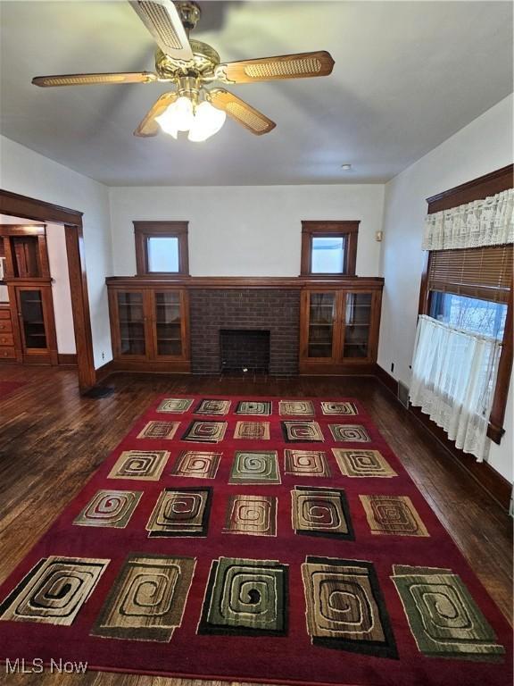 unfurnished living room with dark wood-type flooring, ceiling fan, and a fireplace