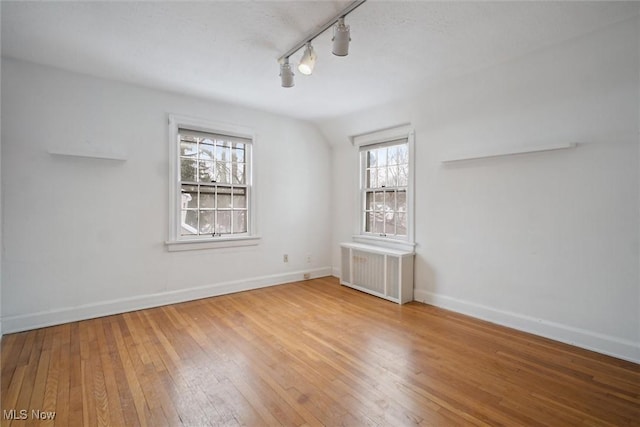 empty room with wood-type flooring, plenty of natural light, radiator, and track lighting