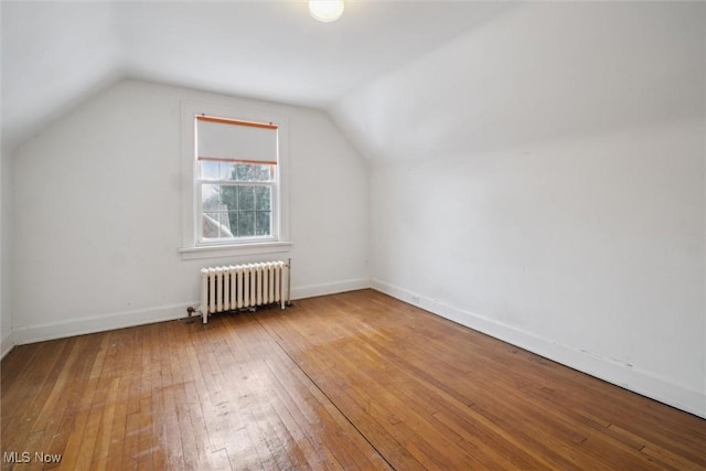 additional living space featuring hardwood / wood-style floors, vaulted ceiling, and radiator heating unit