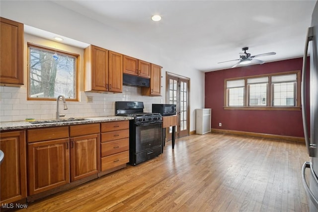 kitchen with sink, backsplash, light hardwood / wood-style floors, black appliances, and light stone countertops