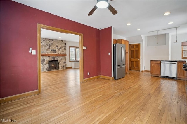 unfurnished living room featuring ceiling fan, a stone fireplace, and light wood-type flooring