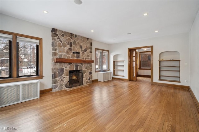 unfurnished living room with radiator, a stone fireplace, a wealth of natural light, and light wood-type flooring