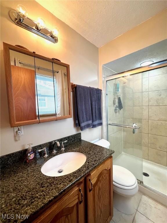 bathroom featuring toilet, a textured ceiling, vanity, a shower with door, and tile patterned flooring