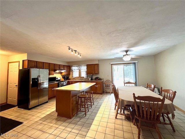 kitchen with light tile patterned flooring, a textured ceiling, appliances with stainless steel finishes, a kitchen breakfast bar, and a kitchen island