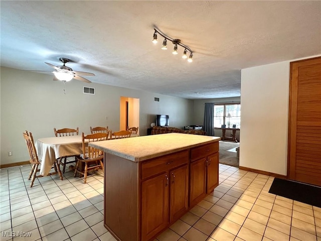 kitchen with ceiling fan, a center island, a textured ceiling, and light tile patterned floors