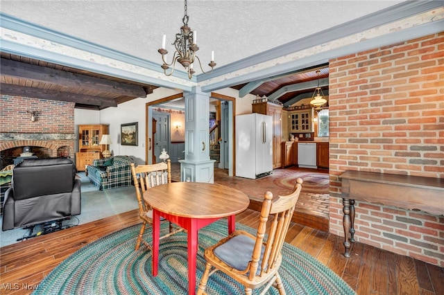 dining space with ornate columns, wood-type flooring, a textured ceiling, brick wall, and beam ceiling