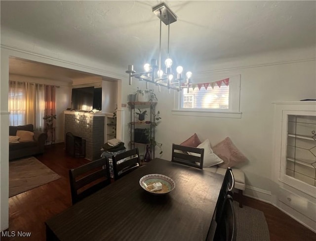 dining room with dark hardwood / wood-style flooring, a chandelier, and a brick fireplace