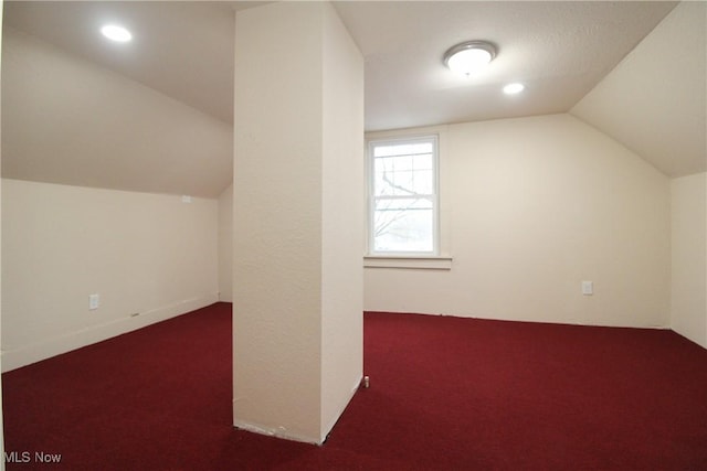 bonus room with dark colored carpet and lofted ceiling