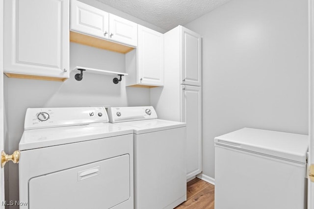 laundry area featuring cabinets, washing machine and dryer, a textured ceiling, and light wood-type flooring