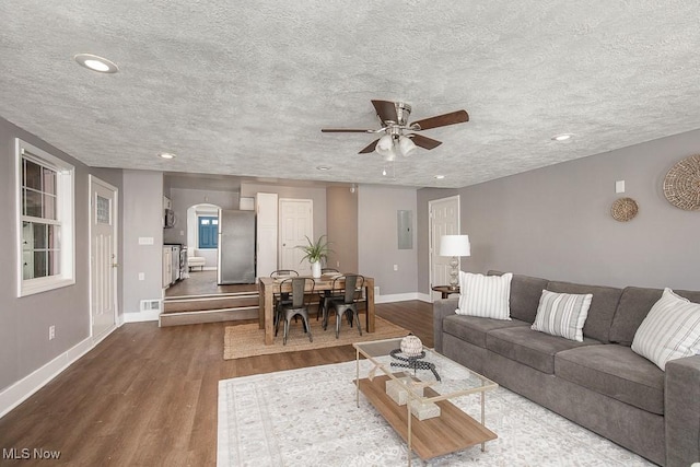 living room featuring ceiling fan, dark wood-type flooring, and a textured ceiling