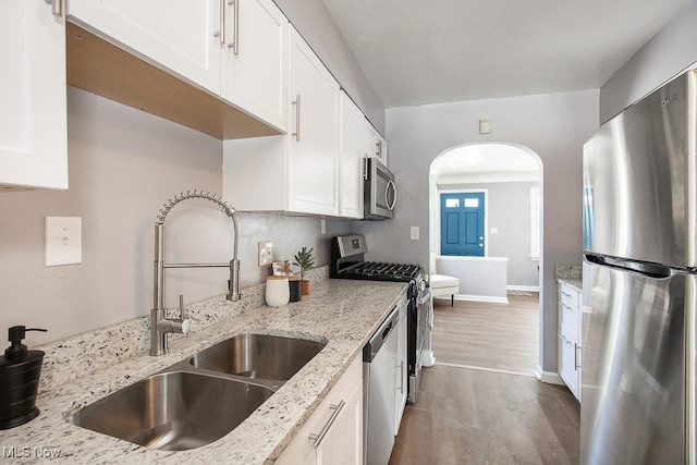 kitchen with sink, hardwood / wood-style flooring, appliances with stainless steel finishes, light stone countertops, and white cabinets