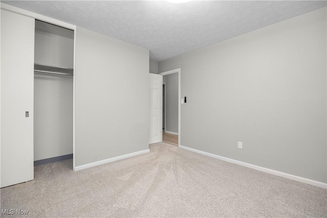 unfurnished bedroom with light colored carpet, a closet, and a textured ceiling