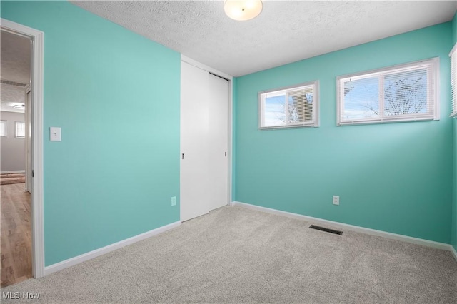 unfurnished bedroom with light colored carpet, a closet, and a textured ceiling