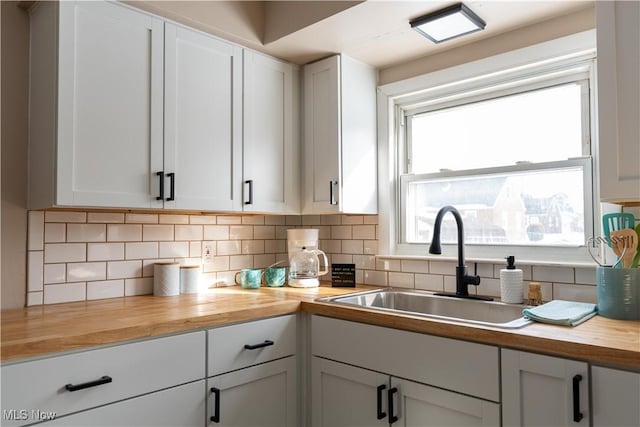 kitchen with backsplash, butcher block counters, sink, and white cabinets