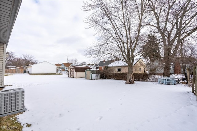 snowy yard featuring central AC unit and a storage unit