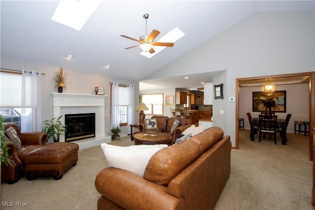 living room with a skylight, high vaulted ceiling, light carpet, ceiling fan, and a fireplace