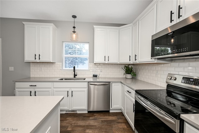 kitchen featuring appliances with stainless steel finishes, white cabinetry, sink, backsplash, and hanging light fixtures