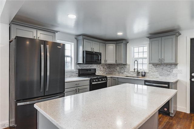 kitchen with sink, backsplash, a center island, black appliances, and light stone countertops