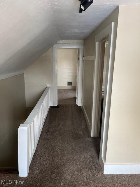 corridor with lofted ceiling and dark carpet