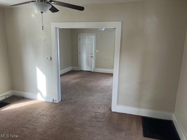 empty room featuring ceiling fan and dark carpet