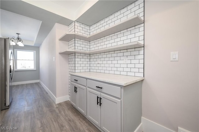 kitchen featuring stainless steel refrigerator, white cabinets, decorative backsplash, light hardwood / wood-style floors, and light stone counters