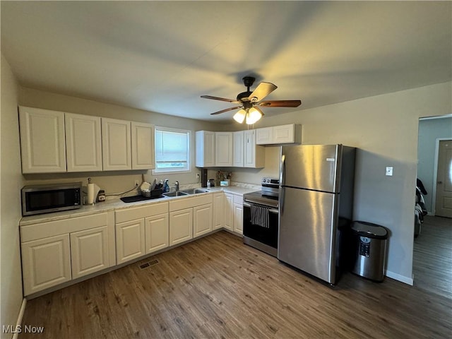 kitchen with appliances with stainless steel finishes, sink, white cabinets, hardwood / wood-style flooring, and ceiling fan