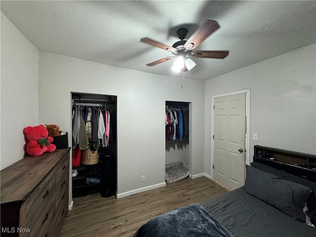 bedroom with two closets, dark wood-type flooring, and ceiling fan