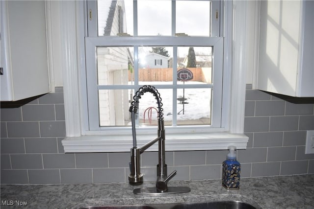 details featuring light stone counters, tasteful backsplash, a sink, and white cabinetry