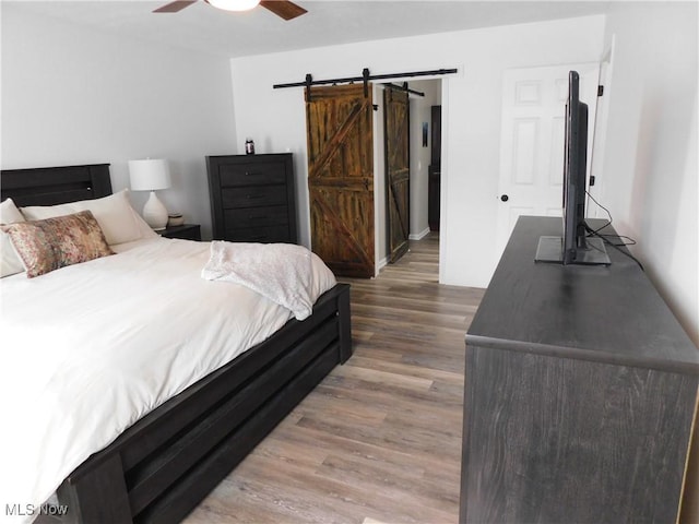 bedroom with ceiling fan, wood-type flooring, and a barn door