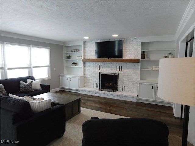 living room featuring wood-type flooring, crown molding, a brick fireplace, a textured ceiling, and built in shelves