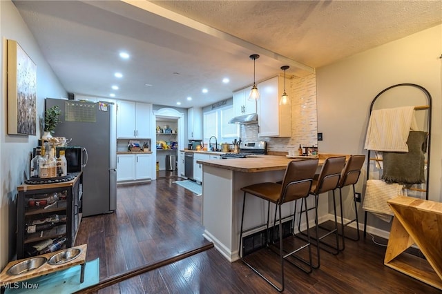 kitchen featuring white cabinetry, stainless steel appliances, decorative light fixtures, and a kitchen bar