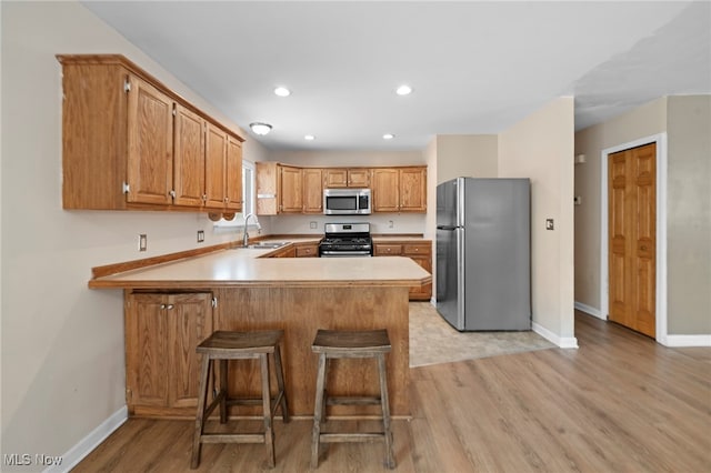 kitchen featuring appliances with stainless steel finishes, a breakfast bar, sink, light hardwood / wood-style floors, and kitchen peninsula