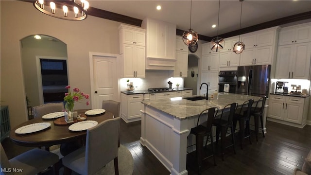 kitchen with pendant lighting, a kitchen island with sink, dark stone countertops, white cabinets, and stainless steel gas stovetop